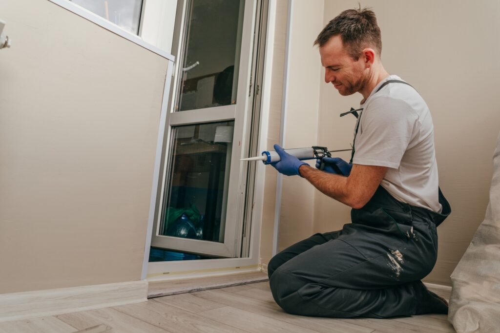 Young man wearing overalls sealing a door